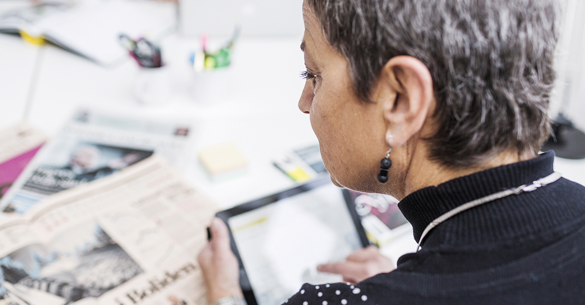 Cropped image of businesswoman using digital tablet with newspapers on desk